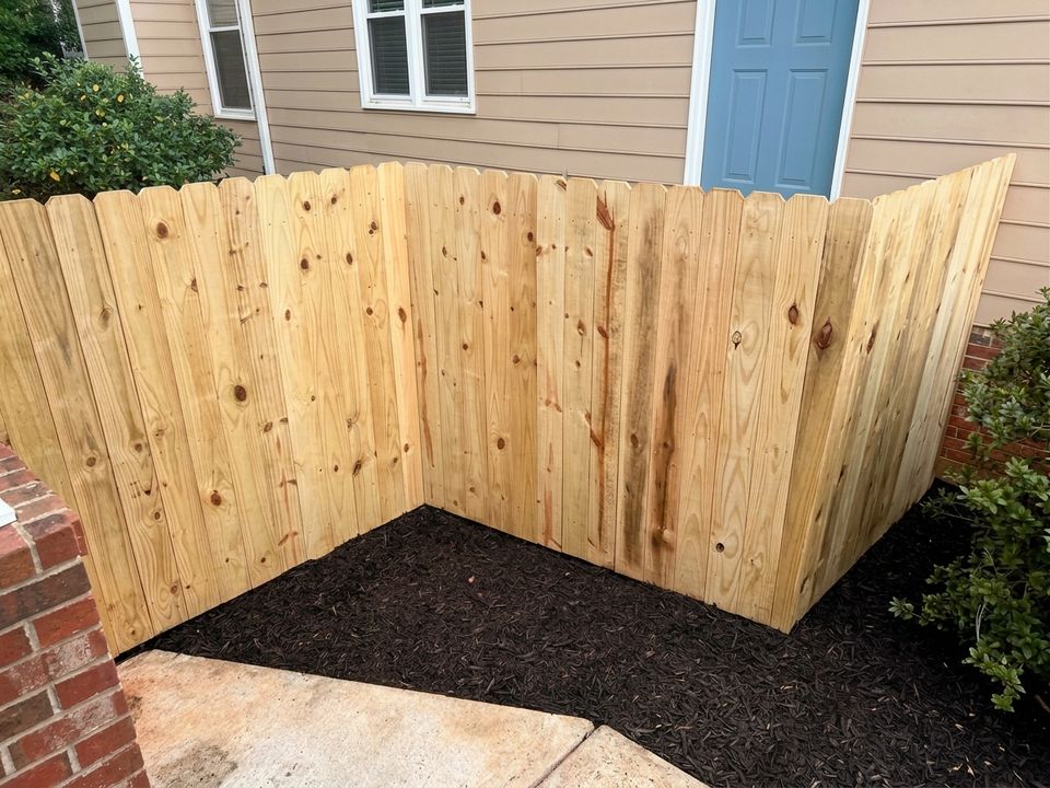 New pressure-treated pine privacy fence enclosing a mulched side yard next to a brick wall